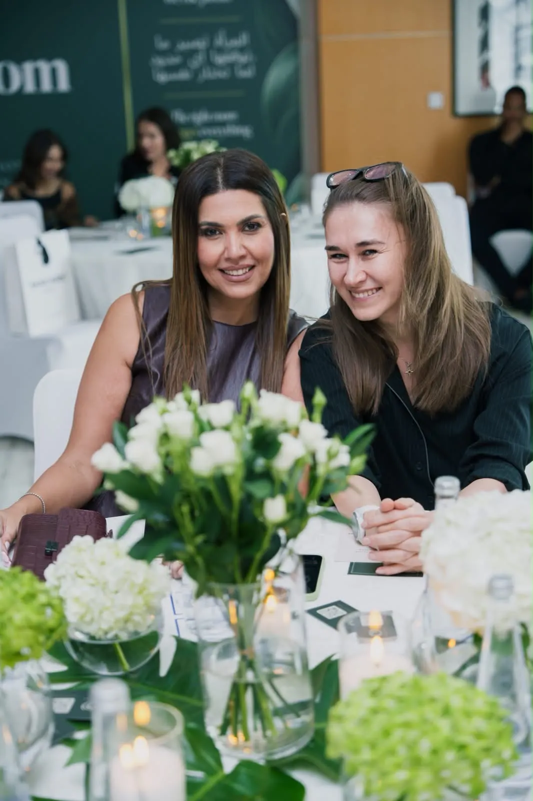 Two women smiling at a lunch table set with white flowers.