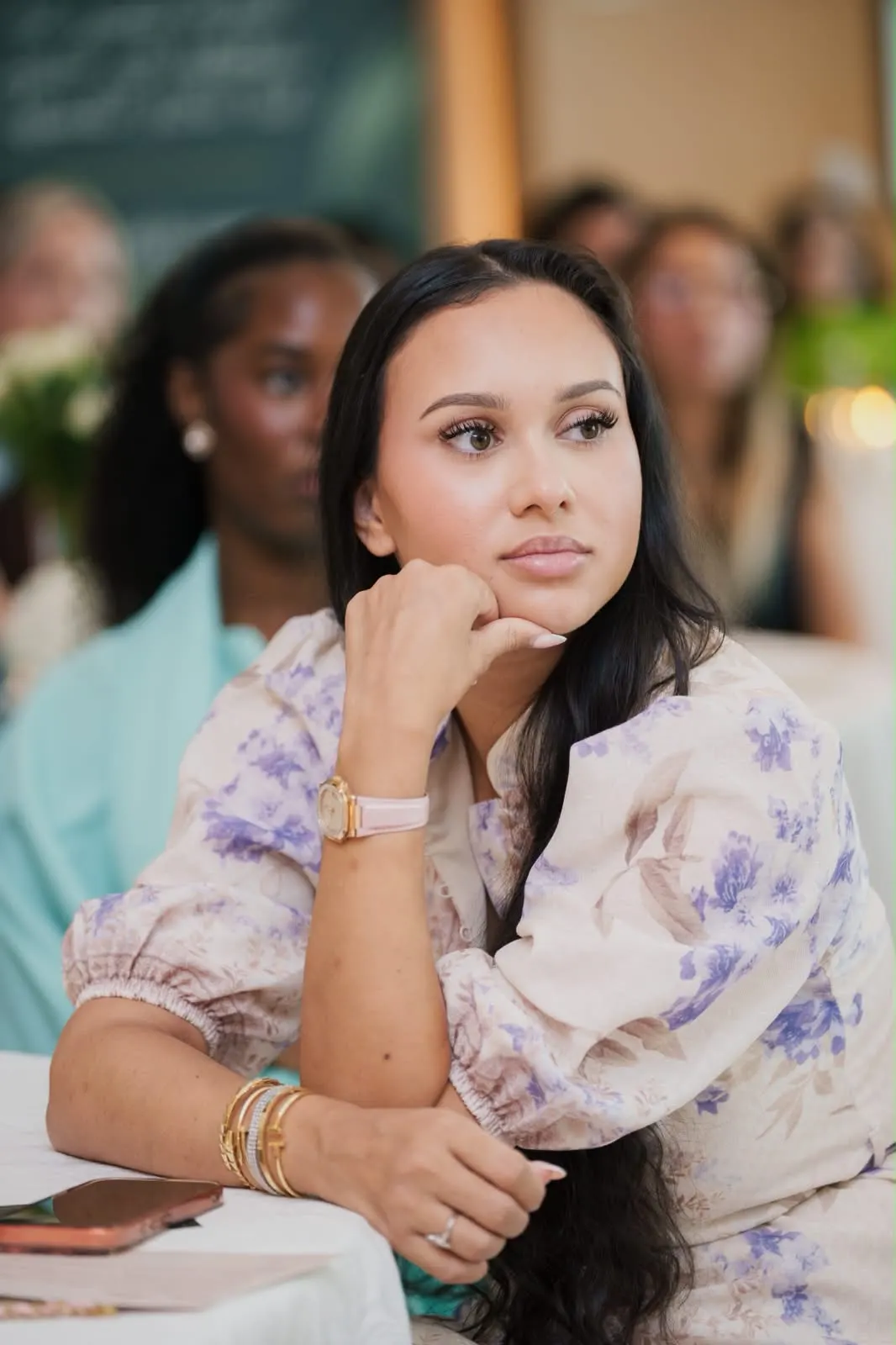 A guest in a floral dress listening, chin resting on her hand.
