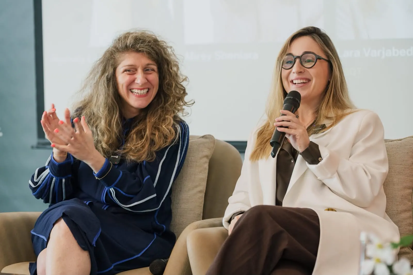 Two panellists laughing on stage, one holding a microphone.